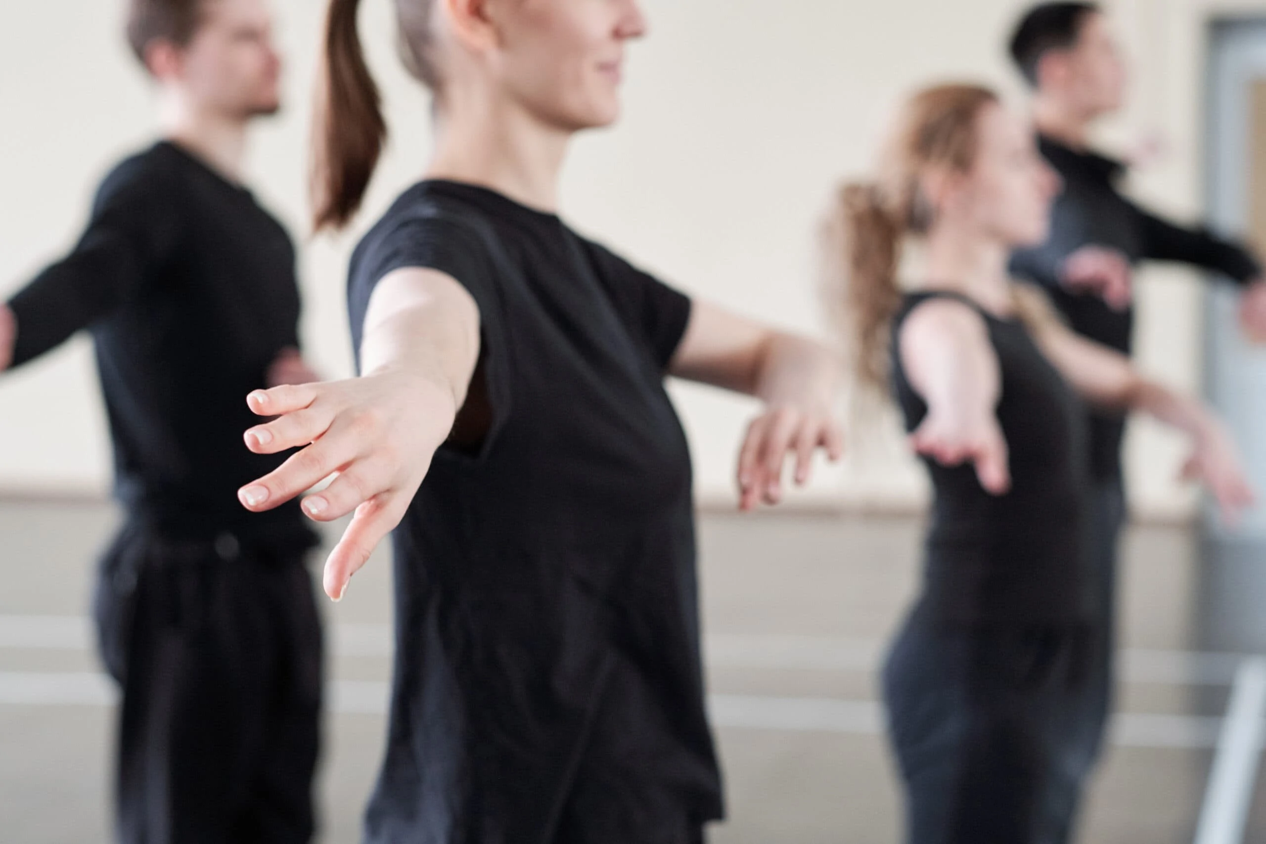 Hand of young active woman in black t-shirt exercising at lesson in dance studio on background of other students